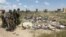 In this image made from video, Iraqi Shi'ite militiamen stand near a mass grave, believed to contain the bodies of Iraqi soldiers killed by Islamic State group militants when they overran Camp Speicher military base last June, in Tikrit, Iraq, April 2, 20
