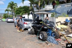 Neighbors clean up debris near the home where a New Year's Eve fireworks explosion killed and injured people, Jan. 1, 2025, in Honolulu.