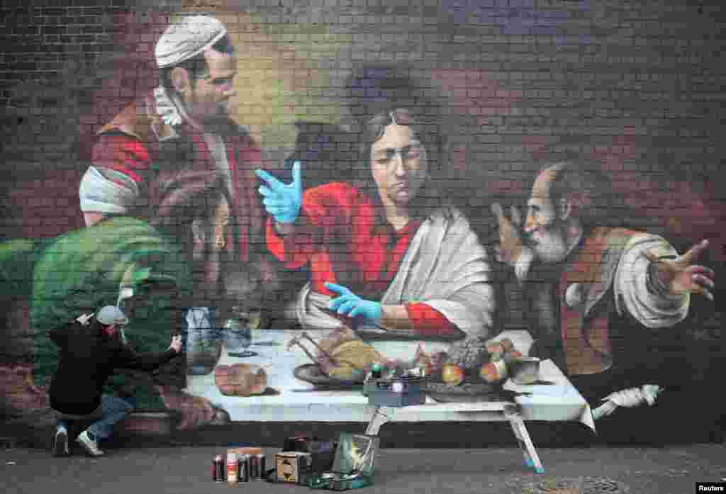 Artist Lionel Stanhope paints a mural in Ladywell depicting the Supper at Emmaus by Caravaggio with added protective gloves, in London.