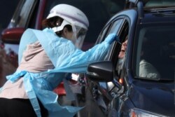 A health care worker tests people at a drive-thru testing station run by the state health department, for people who suspect they have novel coronavirus, in Denver, Colorado, March 11, 2020.