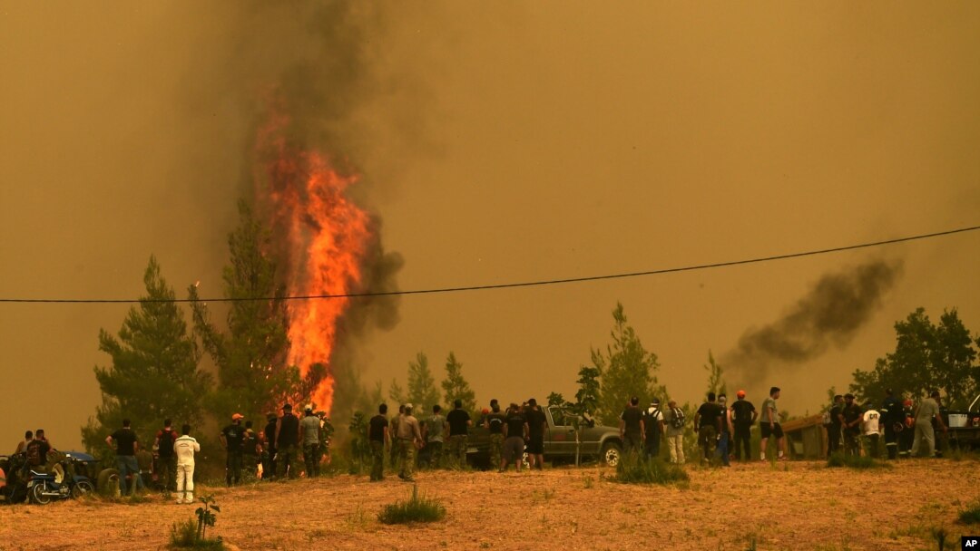Orang-orang menyaksikan kobaran api yang membakar pohon-pohon dalam kebakaran hutan di Desa Avgaria, Pulau Evia, sekitar 184 kilometer (113 mil) utara Athena, Yunani, 9 Agustus 2021.