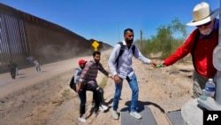 Tom Wingo, de Samaritanos Sin Fronteras, a la derecha, entrega bocadillos y botellas de agua a un grupo de inmigrantes que dicen ser de la India y que acaban de cruzar el muro fronterizo, el 29 de agosto de 2023, en Organ Pipe Cactus National, Arizona, EEUU.