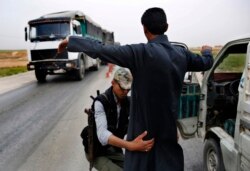 FILE - A Kurdish policeman checks an Arab Syrian man at a checkpoint controlled by the U.S.-backed Syrian Democratic Forces on a highway in Hassakeh province, March 28, 2018.