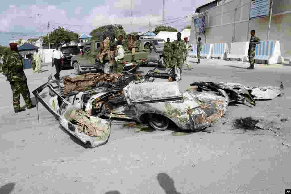 Somali soldiers stand near the wreckage of car bomb that was detonated at the main gate of the presidential palace in Mogadishu, July, 9, 2014.