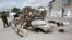 FILE - Somali soldiers stand near the wreckage of car bomb that was detonated at the main gate of the presidential palace in Mogadishu, July, 9, 2014.