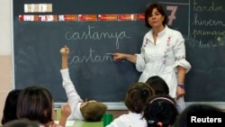 FILE- A teacher points to a blackboard with words in Catalan and in Spanish during a language class at a public school in El Masnou, near Barcelona, Spain.