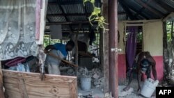 Dos jóvenes limpian una casa gravemente dañada por el terremoto en Chardonnieres, Haití el 18 de agosto de 2021.