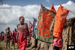 FILE - A young Maasai man wearing traditional clothes and red ochre pigment on his head stands next to ceremonial houses decorated with colourful flags at the ceremonial site during the Eunoto ceremony in a remote area near Kilgoris, Kenya on August 18