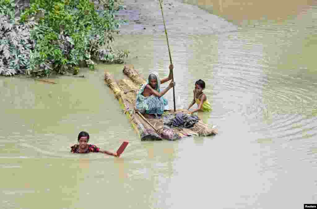 Seorang perempuan lansia mendayung rakit, sementara anak-anak perempuan berusaha melintasi banjir yang melanda desa Laharighat, distrik Morigaon, negara bagian Assam, India.