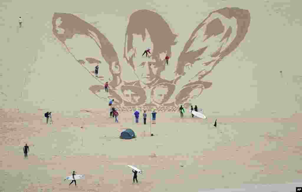 Surfers and sunbathers look on as activists put on the finishing touches as they draw the heads of G7 leaders in the sand on the beach at Newquay, Cornwall, England.