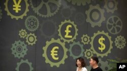 People walk past a mural on a bank showing symbols for American, Chinese and other world currencies in Beijing, July 7, 2018.