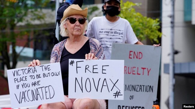 A protestor holds signs outside the Park Hotel, where Serbian tennis player Novak Djokovic is believed to be held, in Melbourne, Australia January 6, 2022.