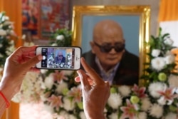 A woman uses a smart phone to take a picture of a portrait of the former chief ideologist and 'Brother Number Two' of Cambodia's Khmer Rouge Nuon Chea during his funeral in Pailin province, Cambodia, August 6, 2019.