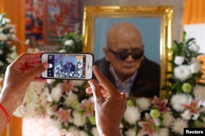 A woman uses a smart phone to take a picture of a portrait of the former chief ideologist and 'Brother Number Two' of Cambodia's Khmer Rouge Nuon Chea during his funeral in Pailin province, Cambodia, August 6, 2019.