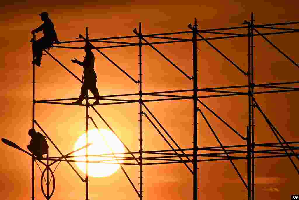 Workers stand on scafolding at sunset in Hanoi, Vietnam.