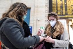 Women wearing protective masks disinfect their hands at the central railway station, after a coronavirus outbreak, in Milan, Italy, Feb. 24, 2020.