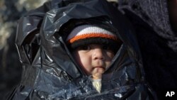 A child is covered in plastic as migrants travel by dinghy to the Greek island of Chios, from the Turkish coast near Cesme, Izmir, Turkey, Nov. 4, 2015. More than 300,000 people have traveled on dinghies and boats from nearby Turkey to Greek islands this 