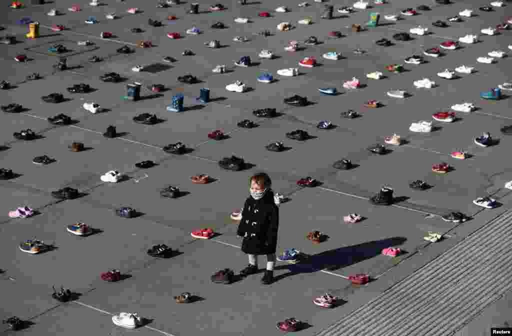A child wearing a face covering is surrounded by shoes, after the group Extinction Rebellion laid out 1,500 pairs of children&#39;s shoes in Trafalgar Square in central London to demand that the government adopts a climate-friendly economic recovery plan.