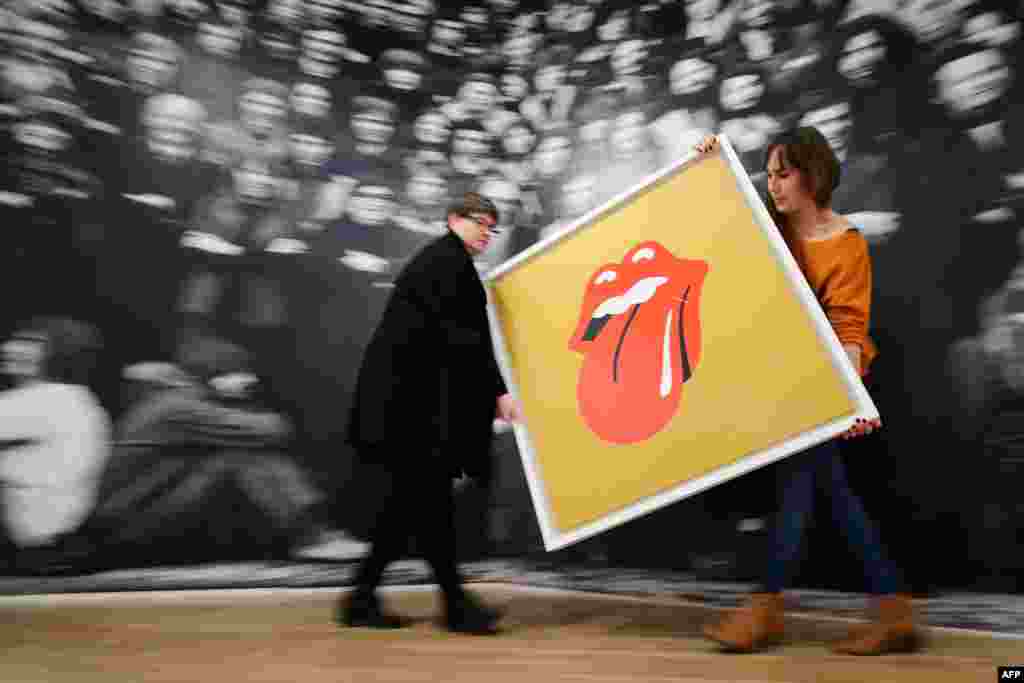 Gallery assistants pose for pictures with John Pasche&#39;s 1971 &#39;Tongue and Lip Design&#39; logo, commissioned by Mick Jagger, at a photocall for a retrospective of students&#39; artwork, titled &quot;GraphicsRCA: Fifty Years&quot; at the Royal College of Arts in London. 