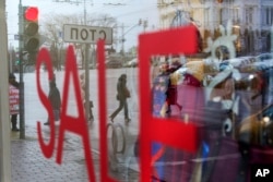 FILE - People reflected in a shop window with a "Sale" sign as they cross a road in downtown Moscow, Feb. 5, 2016.