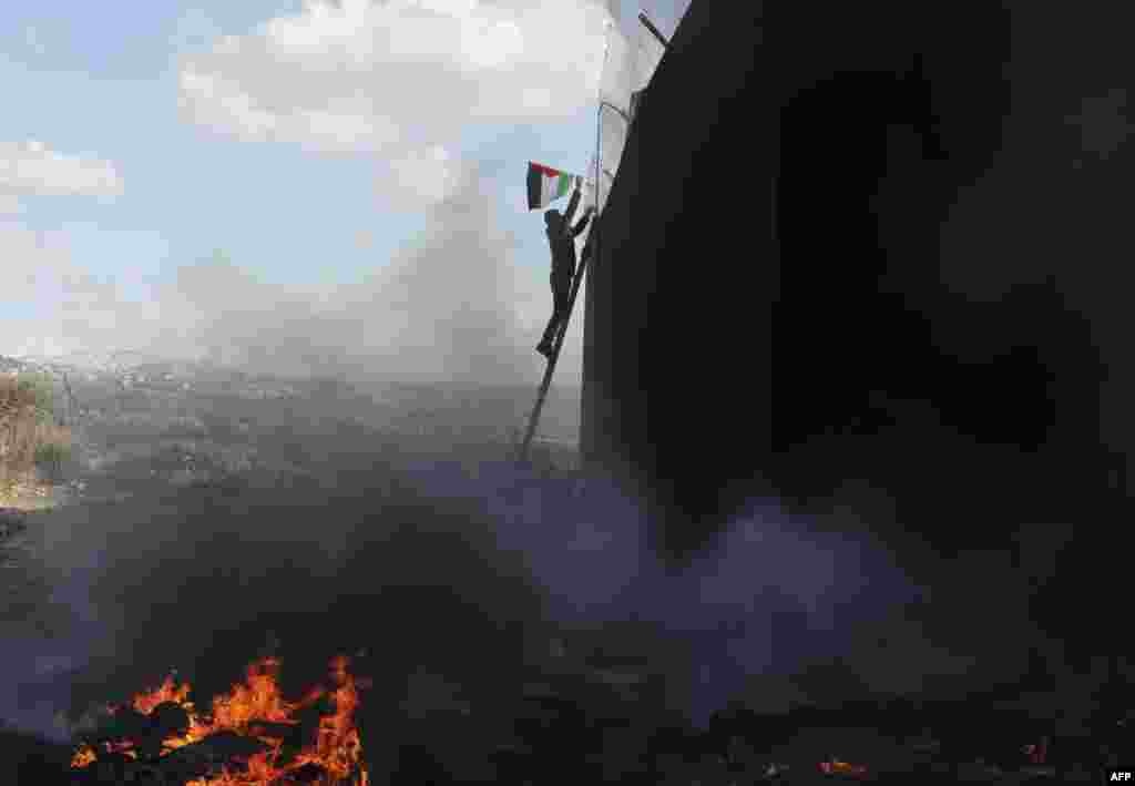 A demonstrator climbing a ladder connects a Palestinian flag to wire on top of Israeli&#39;s controversial separation barrier in the occupied West Bank village of Bilin near Ramallah.