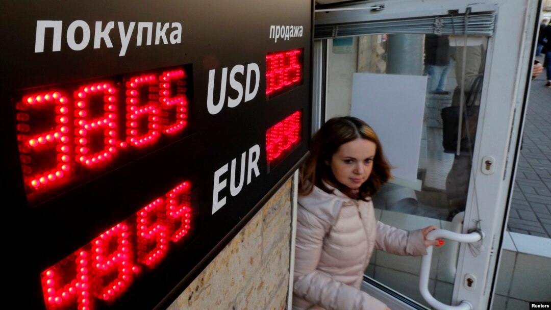 A woman walks out of a building past a board showing currency exchange rates in St. Petersburg, Russia, Sept. 26, 2014. 