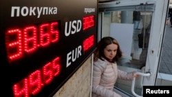 A woman walks out of a building past a board showing currency exchange rates in St. Petersburg, Russia, Sept. 26, 2014. 