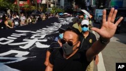 Un manifestante enmascarado levanta la mano para representar las cinco demandas de los manifestantes mientras camina junto a una pancarta que dice "La policía de Hong Kong asesina deliberadamente", el sábado.