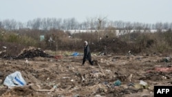 FILE - A man walks among remains of taken down shelters during the dismantling of the southern part of the so-called "Jungle" migrant camp in Calais, northern France, March 10, 2016.