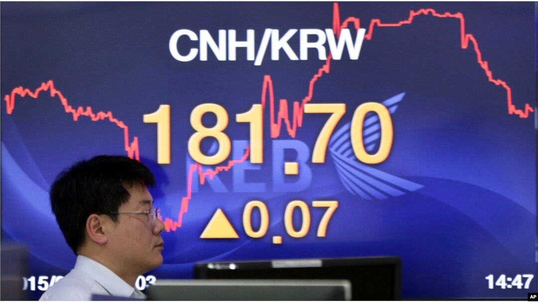An employee walks by a screen showing the foreign exchange rate between the China and South Korea at a bank in Seoul, South Korea, Aug. 13, 2015.