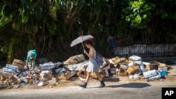FILE - A woman walks by a pile of garbage in the Vedado neighborhood of Havana, Cuba, Oct. 20, 2018.