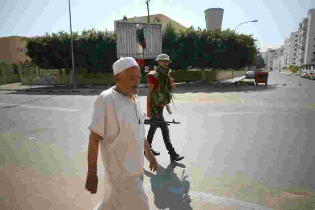 يک رزمنده محلی با پيرمردی در ردای سنتی به پست بازرسی در مرکز طرابلس نزديک می شوند