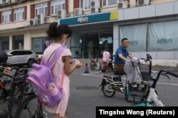 FILE - A girl carrying a schoolbag stands near an outlet of private educational services provider New Oriental Education and Technology Group in Beijing, China July 26, 2021. (REUTERS/Tingshu Wang)