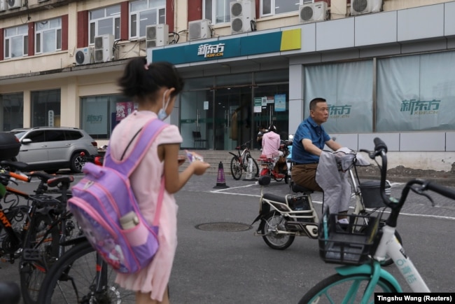 FILE - A girl carrying a schoolbag stands near an outlet of private educational services provider New Oriental Education and Technology Group in Beijing, China July 26, 2021. (REUTERS/Tingshu Wang)