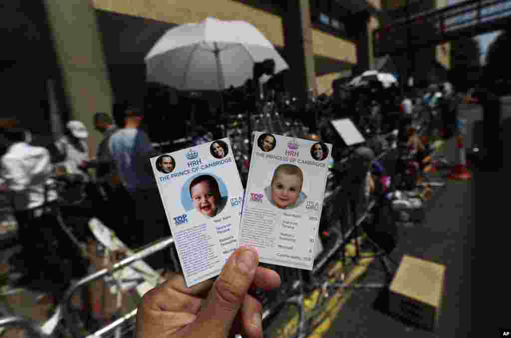 Cards depicting the 'royal baby,' either as a boy or a girl, made as a publicity stunt by a games company, are pictured. Members of the media waiting across from St. Mary's Hospital are seen in the background.