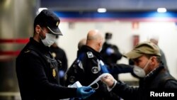 Polisi Spanyol membagikan masker di sebuah stasiun kereta metro di Madrid, Senin (13/4). 