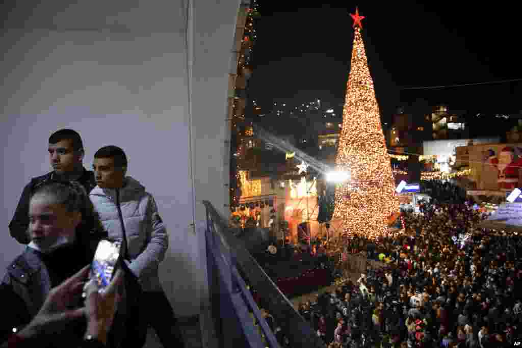 Pessoas reúnem-se no exterior de uma igreja grega ortodoxa em Nazaré, Israel para ver a iluminação da Árvore de Natal. 12 Dezembro 2021