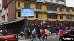 Pedestrians walk past a sign reading "Ebola disease outbreak" outside the Ministry of Finance in Monrovia, Liberia, Jan. 12, 2015.