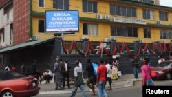 Pedestrians walk past a sign reading "Ebola Disease Outbreak" outside the Ministry of Finance in Monrovia, Liberia, Jan. 12, 2015.