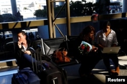 A passenger, left, waits in Los Angeles International Airport for his girlfriend, who was born in Iran but holds a Canadian passport and had not been allowed entry to the U.S. after vacationing in Thailand. Meanwhile, an attorney works to help family members of Sarah Saedian, center right, both effected by the travel ban at Los Angeles International Airport, Jan. 28, 201