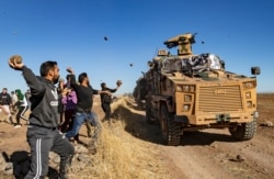 FILE - Kurdish demonstrators hurl rocks at a Turkish military vehicle during a joint Turkish-Russian patrol near the town of Al-Muabbadah in the northeastern part of Hassakah on the Syrian border with Turkey, Nov. 8, 2019.