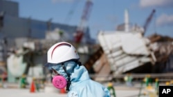 FILE - A Tokyo Electric Power Co. (TEPCO) employee, wearing a protective suit and a mask, walks in front of the No. 1 reactor building at the tsunami-crippled Fukushima Dai-ichi nuclear power plant in Okuma, Fukushima Prefecture, northeastern Japan, Wedne