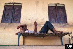 FILE - A man browses a phone while lying on a straw cot bed outside a classroom at a school that has been transformed into a shelter for people displaced by conflict in Sudan's northern border town of Wadi Halfa near Egypt on September 11, 2023.