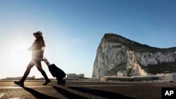 Seorang perempuan berjalan di wilayah Spanyol dekat perbatasan dengan wilayah Inggris di Gibraltar, dengan batu karang Gibraltar tampak di belakang, di kota La Linea de la Concepcion, Spanyol (foto: dok). 