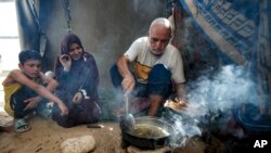 Hassan Nofal, desno, koji je raseljen zbog izraelskog bombardovanja pojasa Gaze, priprema ručak sa svojom porodicom u improvizovanom šatorskom kampu u Khan Younisu, južnom pojasu Gaze, u četvrtak, 4. jula 2024.