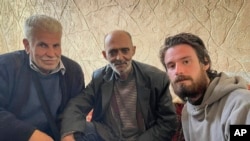 In this photo provided by the Syrian Emergency Task Force, American Travis Timmerman, right, sits with Mosaed al-Rifai, center, who found him in the Syrian desert, and the owner of the house where he took refuge, left, name not available, in Damascus, Syria, Dec. 12, 2024. 