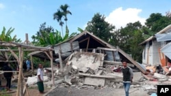 Warga berjalan di dekat rumah yang rusak akibat gempa di desa Sajang, Sembalun, Lombok timur, Minggu, 29 Juli.