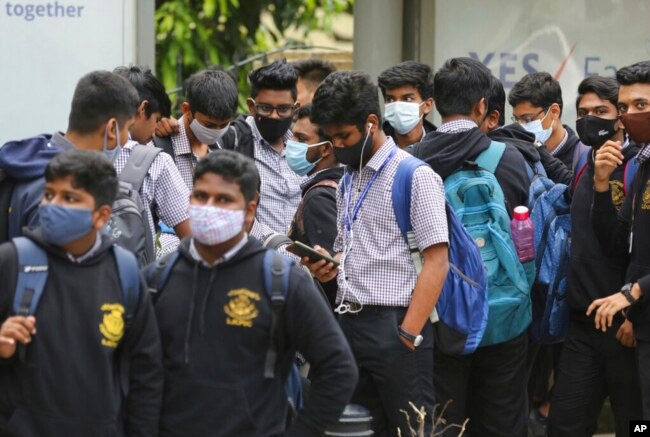 School students wearing face masks as a precaution against COVID-19 wait at a bus stop in Bengaluru, India, Nov. 30, 2021.