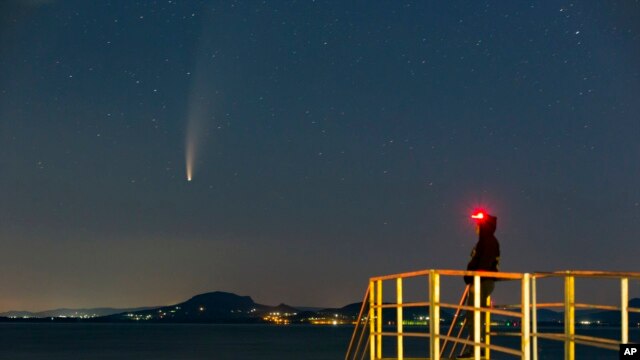 de komeet Neowise of C/2020 F3 wordt gezien voor zonsopgang boven Balatonmariafurdo, Hongarije, dinsdag 14 juli 2020. Het passeerde het dichtst aan de zon op 3 juli en zijn dichtste benadering aan de aarde zal op 23 juli plaatsvinden. (Gyorgy Varga / MTI via AP)