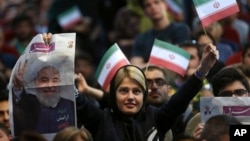 A pro-reform Iranian woman who supports President Hassan Rouhani for the May 19 presidential election holds his picture, on special edition of Shargh daily, and Iranian flag in a campaign rally in Tehran, Iran, April, 29, 2017. 